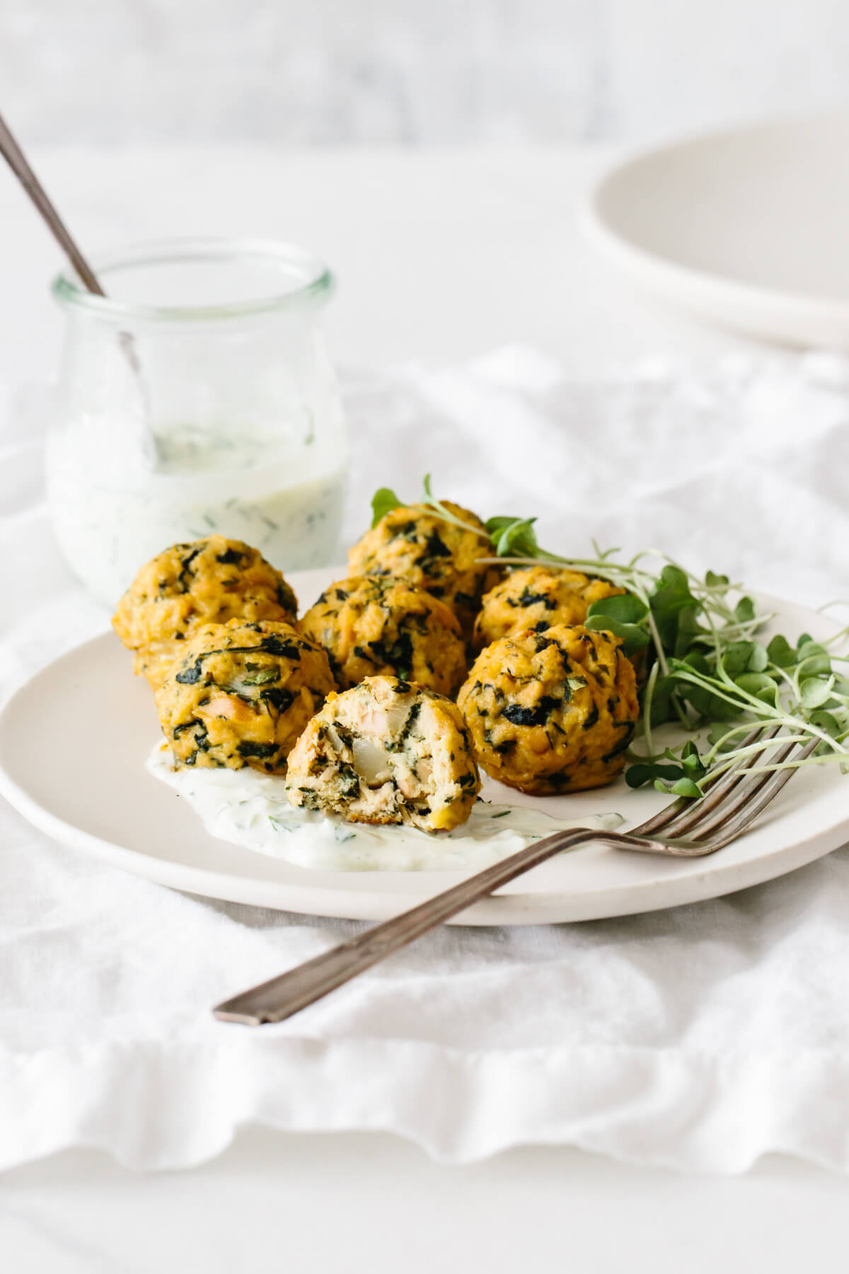 A plate of tuna meatballs garnished with tzatziki and micro greens with one half eaten .