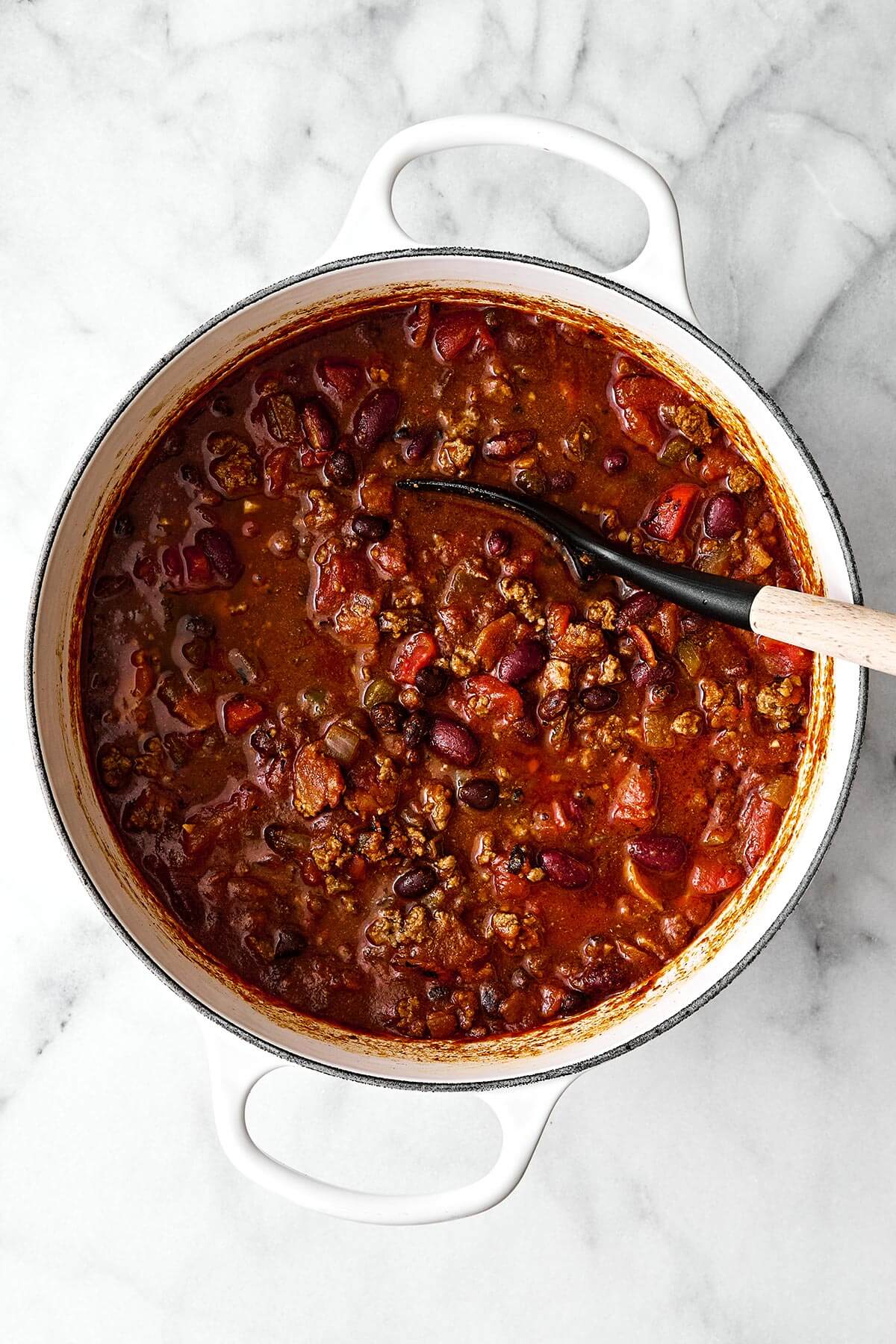 A white pot of chili with a spoon.
