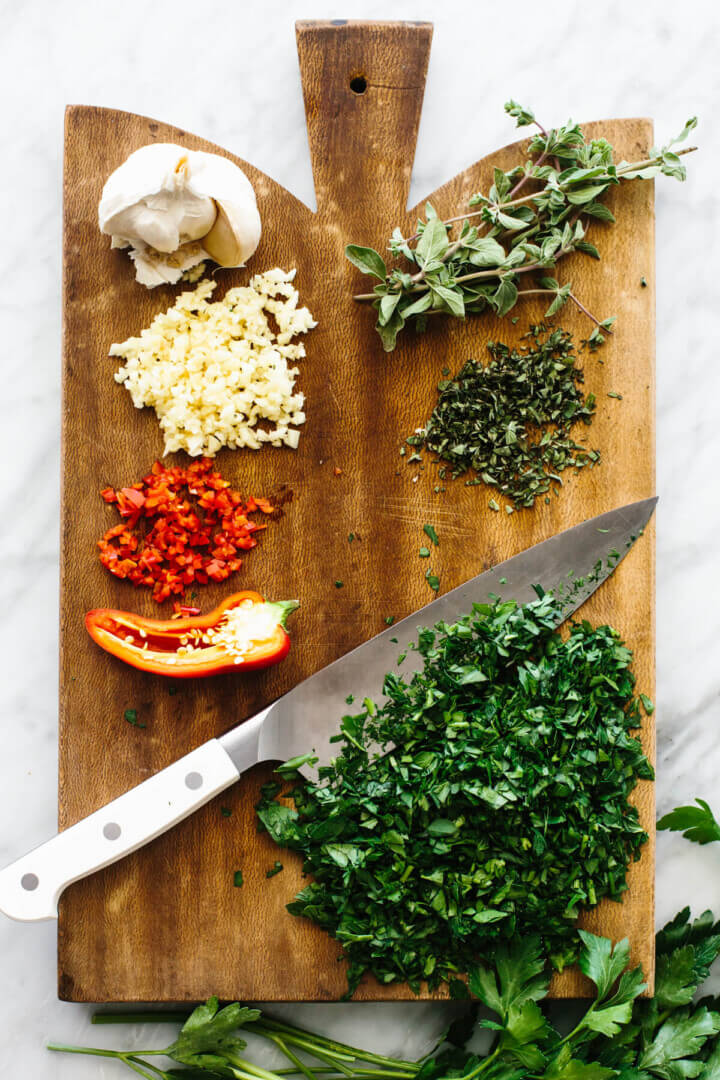 Chopping chimichurri sauce ingredients on a wooden board