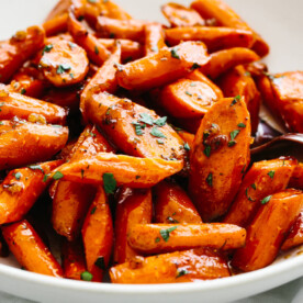 A bowl of honey glazed carrots with a spoon.