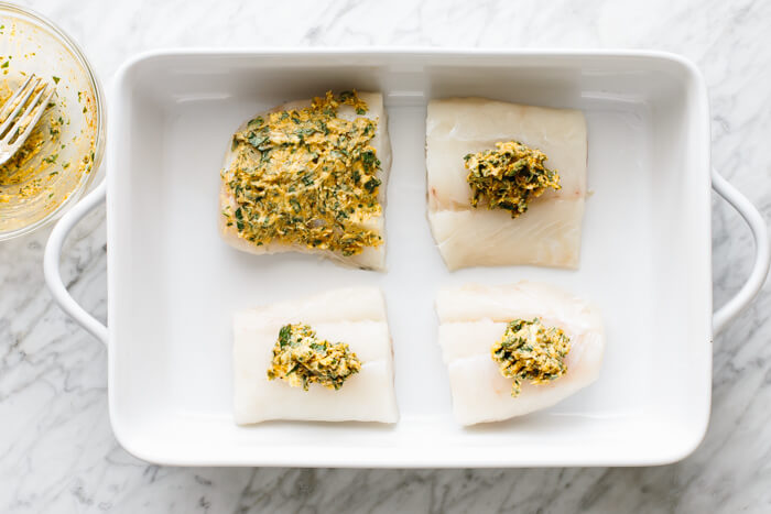 Adding garlic herb butter to cod fillets.
