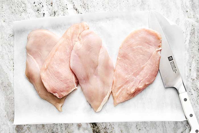 Sliced chicken breasts on parchment paper.