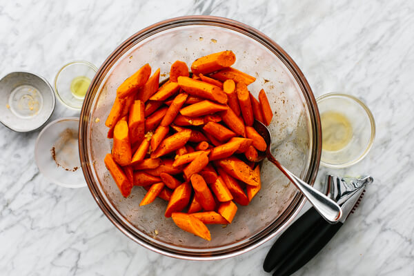 Honey glazed carrots being tossed in a glass bowl.