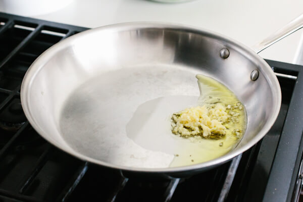 Heating garlic and oil in a pan for garlic sauteed spinach.