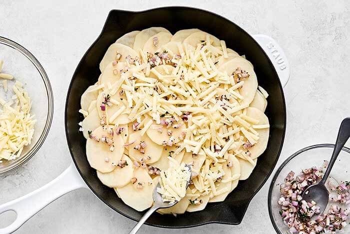 Layering scalloped potato ingredients in a pan.