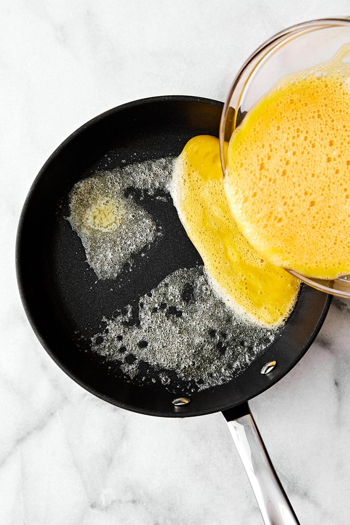 Adding whisked eggs into a pan.