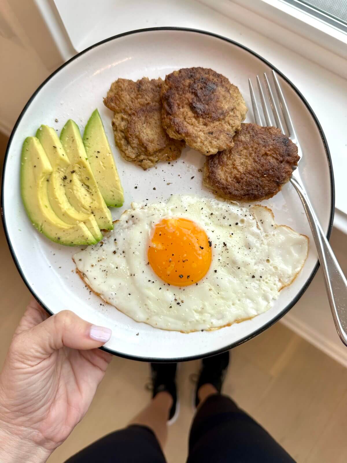 A plate of chicken breakfast sausage, fried egg, and sliced avocado.