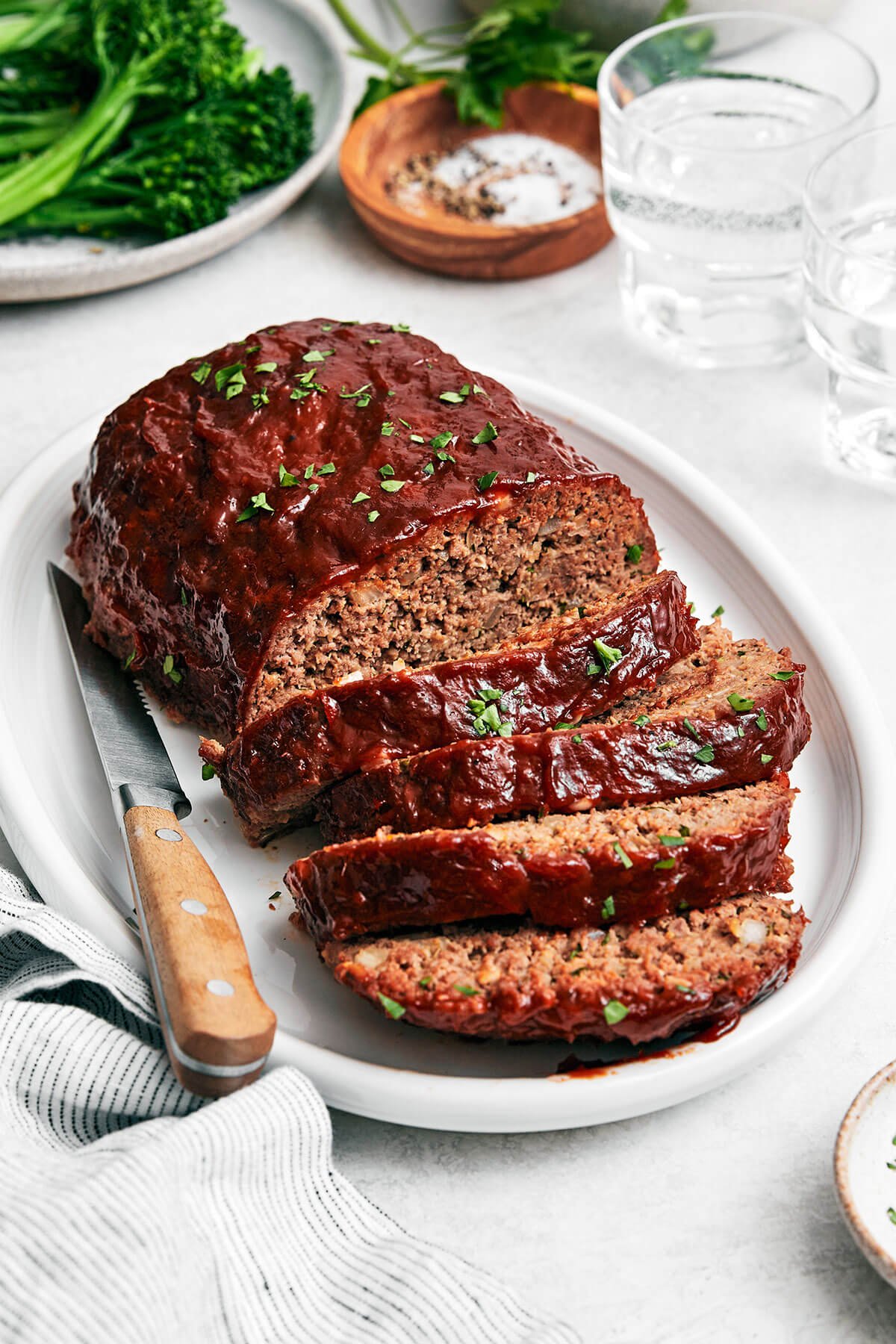 Here's my secret to the best classic meatloaf recipe! It's tender and moist, layered with flavor, and brushed with a tasty meatloaf sauce! Sliced meatloaf on a platter.