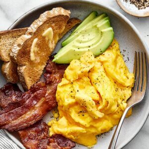 Scrambled eggs with bacon, avocado, and toast.