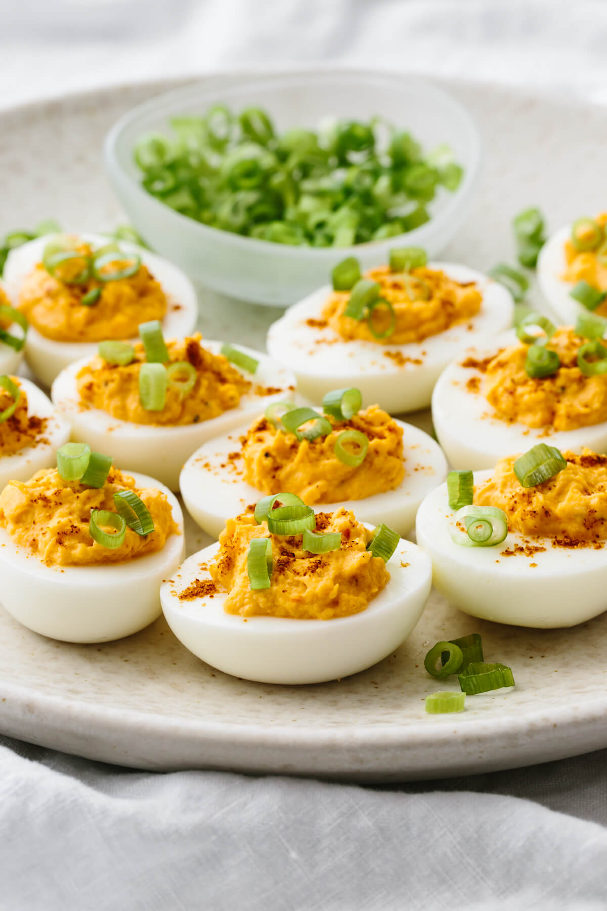 Spicy deviled eggs next to a bowl of green onions.